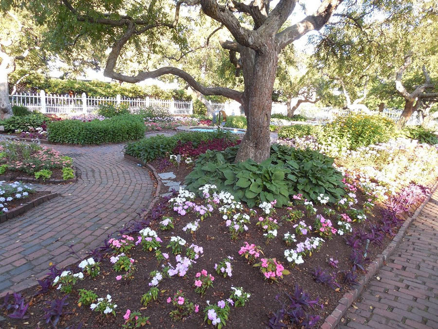 Garden with brick pathway and colorful flowers under large oak trees