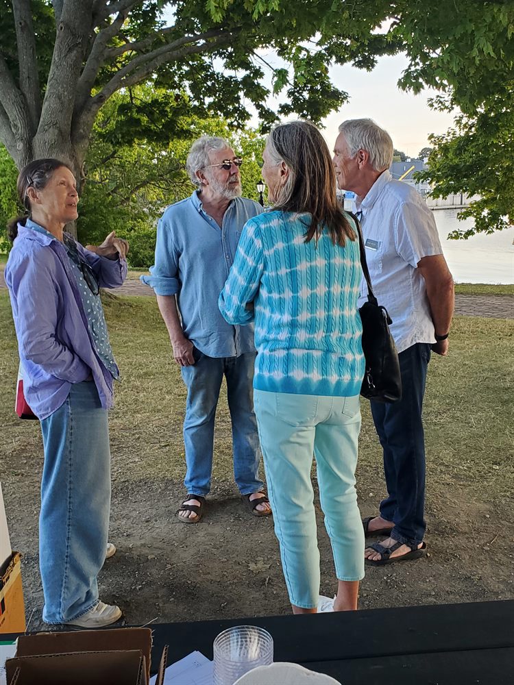 Four attendees talking together under the maple trees beside the water